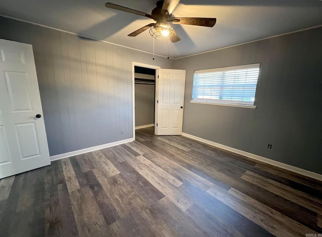 unfurnished bedroom featuring dark hardwood / wood-style flooring, ornamental molding, ceiling fan, wooden walls, and a closet