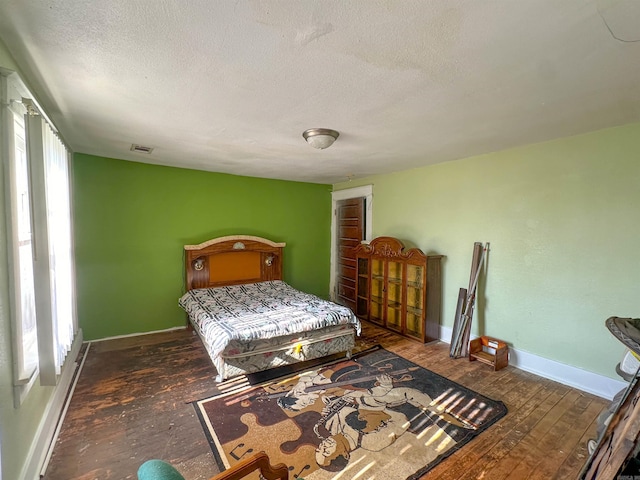 bedroom featuring multiple windows, dark wood-type flooring, and a textured ceiling