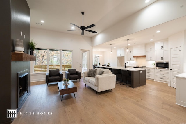 living room with ceiling fan with notable chandelier, light hardwood / wood-style flooring, and sink