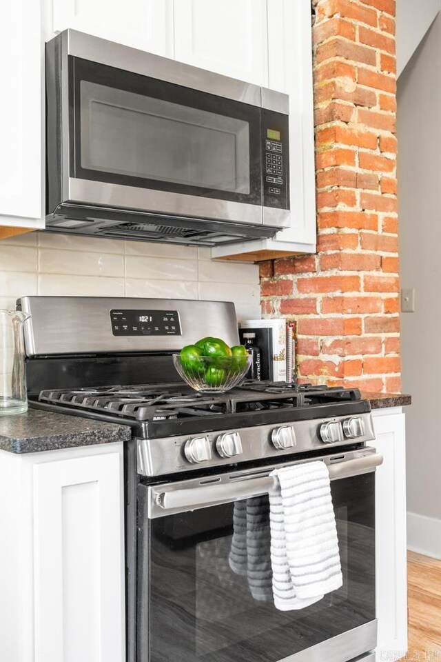 kitchen with dark stone counters, light hardwood / wood-style floors, decorative backsplash, white cabinets, and appliances with stainless steel finishes