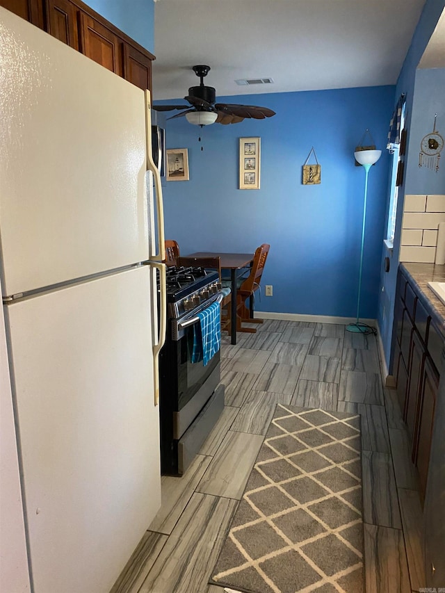 kitchen with stainless steel gas range oven, ceiling fan, white refrigerator, and light hardwood / wood-style floors