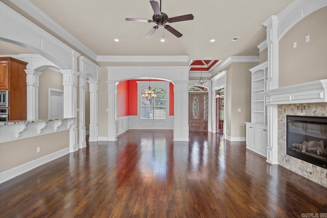 unfurnished living room featuring dark hardwood / wood-style flooring, ornate columns, ceiling fan with notable chandelier, crown molding, and a fireplace