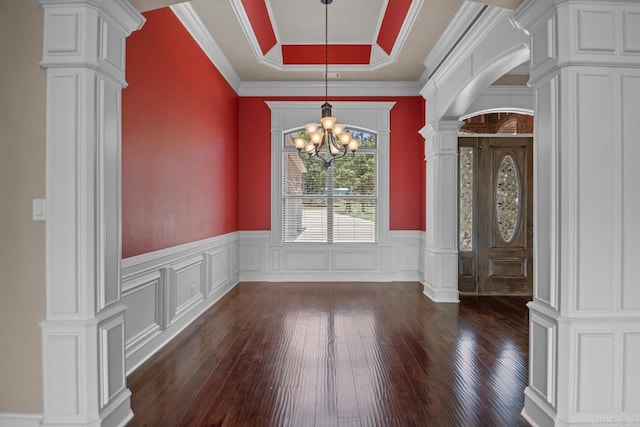 unfurnished dining area with crown molding, a tray ceiling, a notable chandelier, dark hardwood / wood-style flooring, and decorative columns