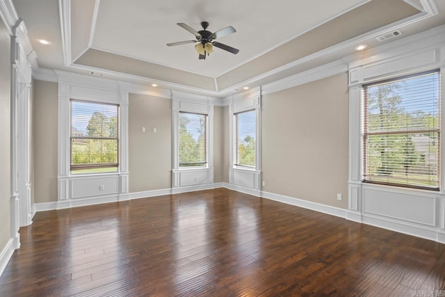 empty room featuring a raised ceiling, dark hardwood / wood-style flooring, ceiling fan, and plenty of natural light