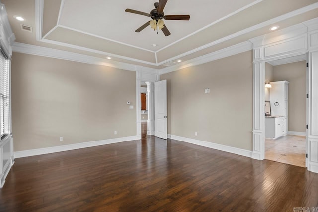 spare room with ceiling fan, dark wood-type flooring, decorative columns, a tray ceiling, and ornamental molding