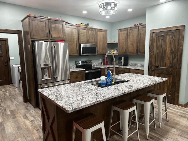 kitchen featuring a center island with sink, light wood-type flooring, dark brown cabinetry, and appliances with stainless steel finishes