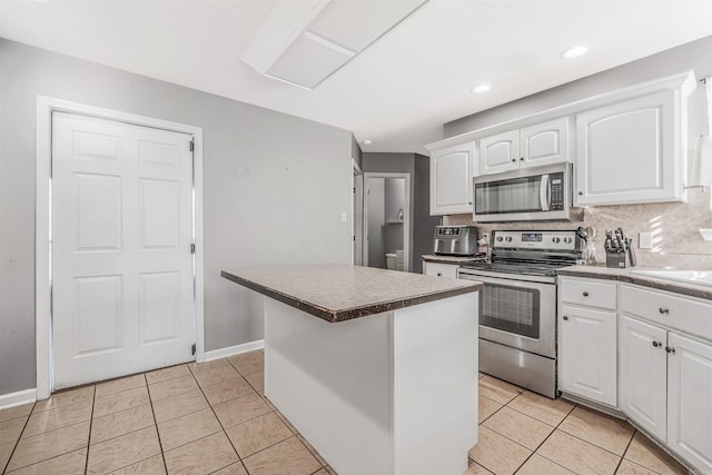 kitchen with appliances with stainless steel finishes, tasteful backsplash, light tile patterned floors, white cabinets, and a kitchen island