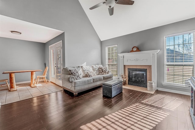 living room featuring a tiled fireplace, ceiling fan, hardwood / wood-style floors, and high vaulted ceiling