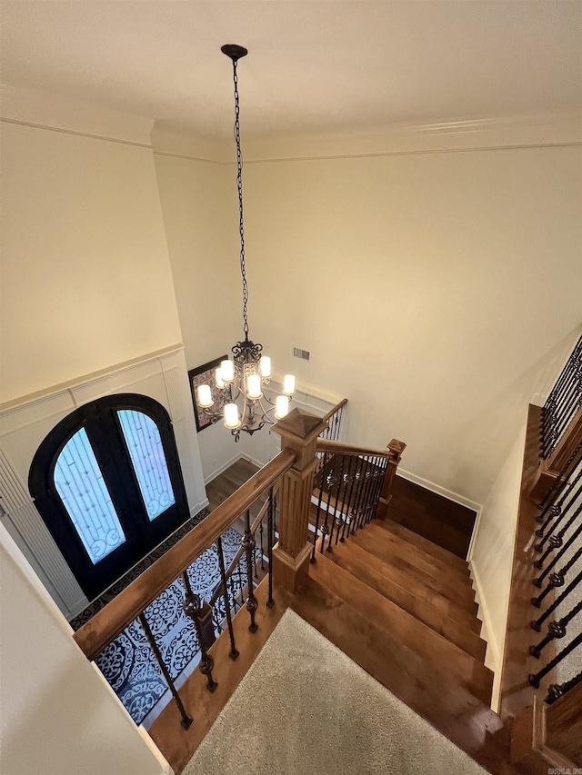 staircase with a towering ceiling, an inviting chandelier, and hardwood / wood-style flooring