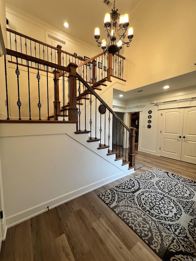 foyer featuring wood-type flooring, a towering ceiling, ornamental molding, and a notable chandelier