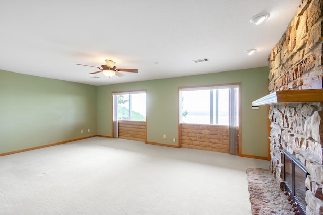 unfurnished living room featuring carpet flooring, a stone fireplace, and ceiling fan