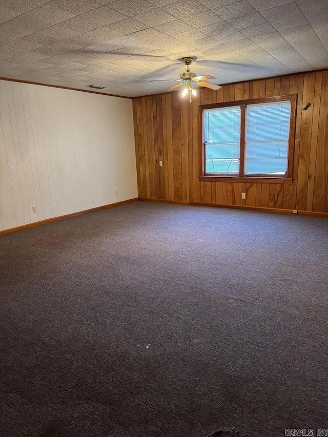 carpeted spare room with ceiling fan and wood walls