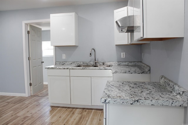 kitchen with white cabinets, light stone countertops, sink, and light hardwood / wood-style flooring