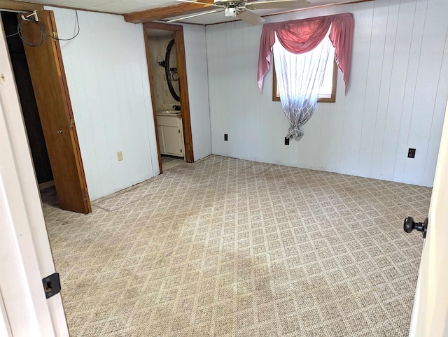 basement with light colored carpet, ceiling fan, and wood walls