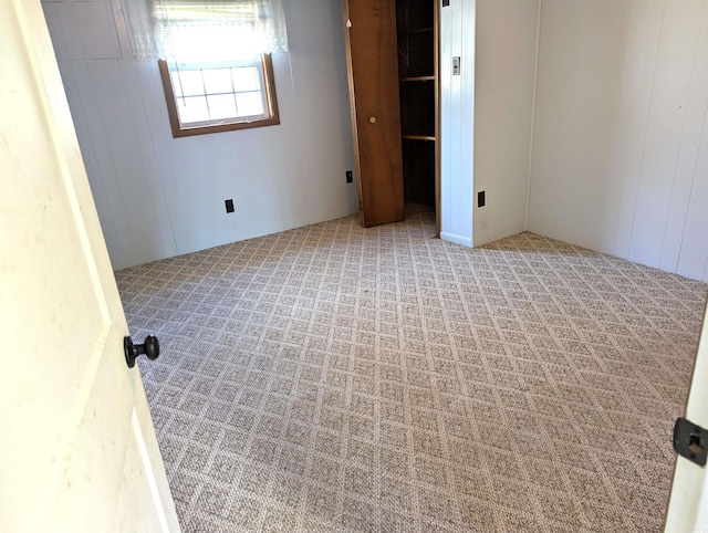 unfurnished bedroom featuring light colored carpet, wooden walls, and a closet