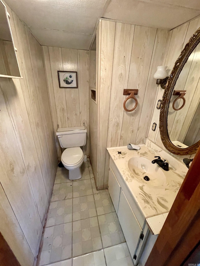 bathroom with vanity, wooden walls, a textured ceiling, and toilet