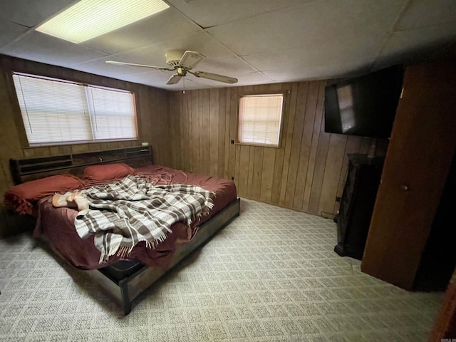 bedroom featuring light colored carpet, a drop ceiling, ceiling fan, and wood walls