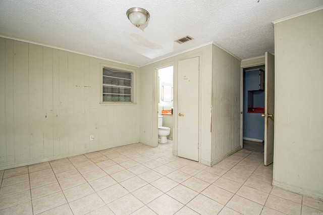 empty room with light tile patterned floors, a textured ceiling, wooden walls, and ornamental molding