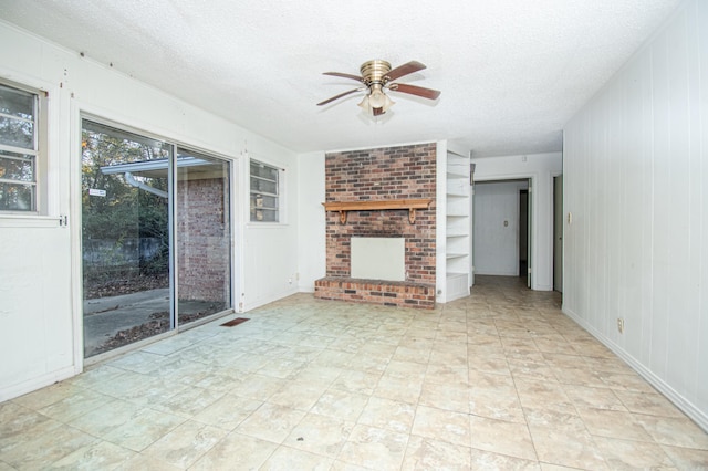 unfurnished living room featuring wood walls, ceiling fan, built in features, a textured ceiling, and a fireplace