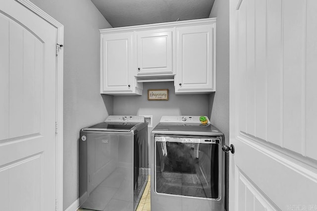 clothes washing area featuring cabinets, light tile patterned floors, and washing machine and dryer