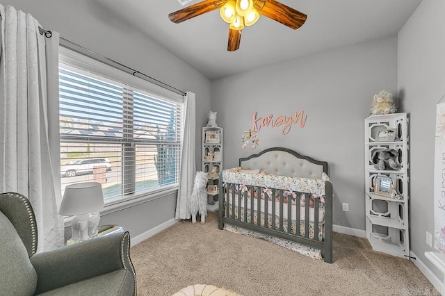 carpeted bedroom with ceiling fan and a nursery area