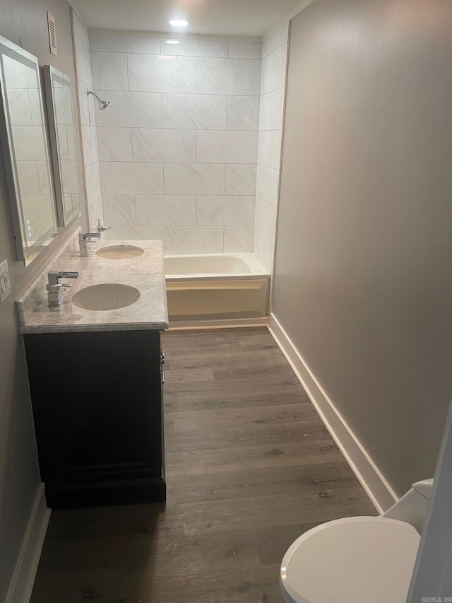 full bathroom featuring hardwood / wood-style floors, vanity, tiled shower / bath combo, and toilet