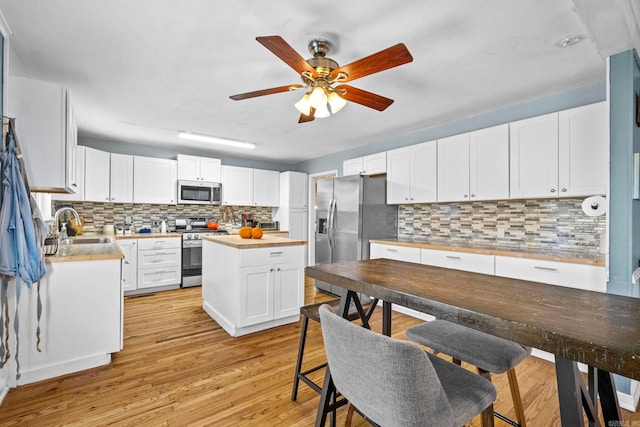 kitchen featuring sink, appliances with stainless steel finishes, tasteful backsplash, light hardwood / wood-style floors, and white cabinetry