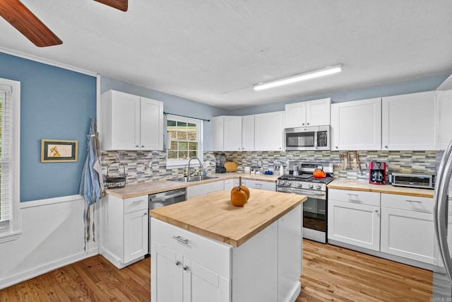 kitchen with wooden counters, stainless steel appliances, white cabinetry, and sink