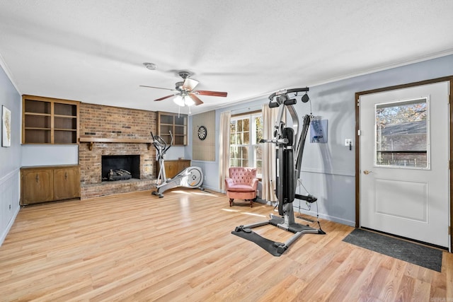 exercise room with crown molding, light wood-type flooring, a textured ceiling, and a brick fireplace