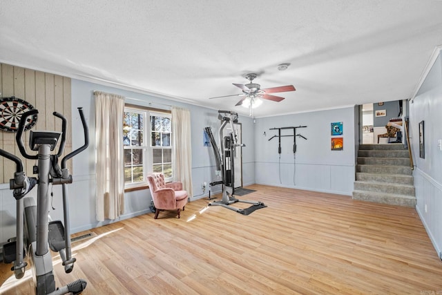 exercise room featuring ceiling fan, crown molding, light wood-type flooring, and a textured ceiling