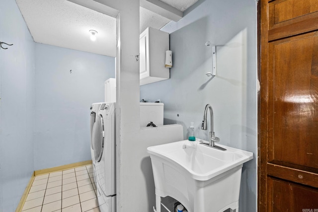 clothes washing area with washing machine and clothes dryer, sink, cabinets, a textured ceiling, and light tile patterned flooring