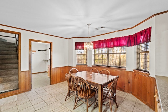 carpeted dining room with wood walls, ornamental molding, and a chandelier