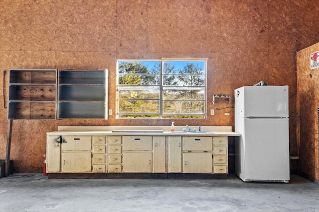 kitchen featuring cream cabinets, white refrigerator, sink, and concrete floors