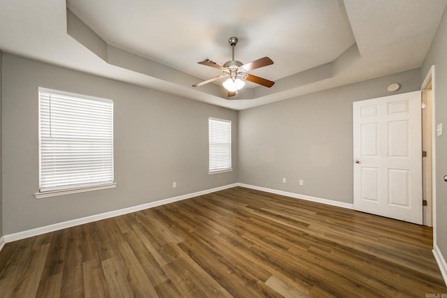 unfurnished room with dark hardwood / wood-style floors, ceiling fan, a raised ceiling, and a wealth of natural light