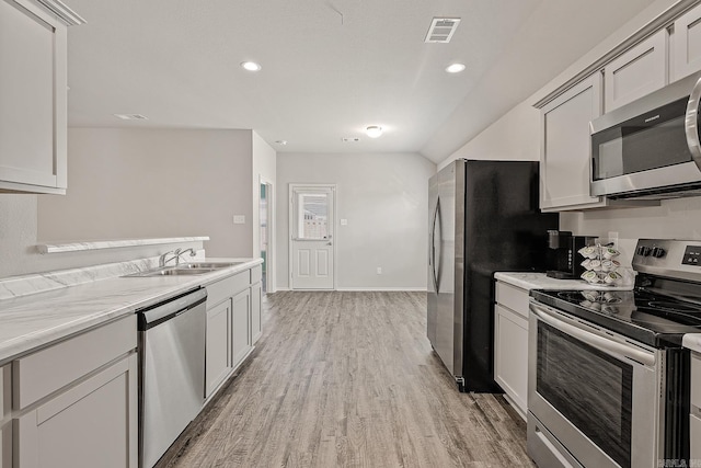 kitchen featuring sink, light hardwood / wood-style flooring, light stone counters, and appliances with stainless steel finishes