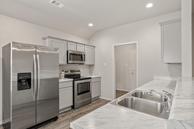 kitchen featuring appliances with stainless steel finishes, light stone counters, sink, hardwood / wood-style flooring, and lofted ceiling