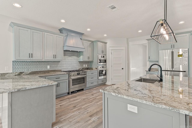 kitchen featuring light wood-type flooring, premium appliances, sink, pendant lighting, and gray cabinets