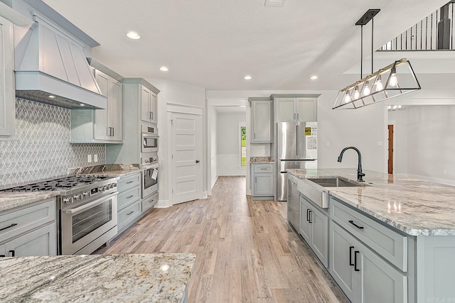 kitchen featuring pendant lighting, premium range hood, gray cabinets, light hardwood / wood-style floors, and stainless steel appliances