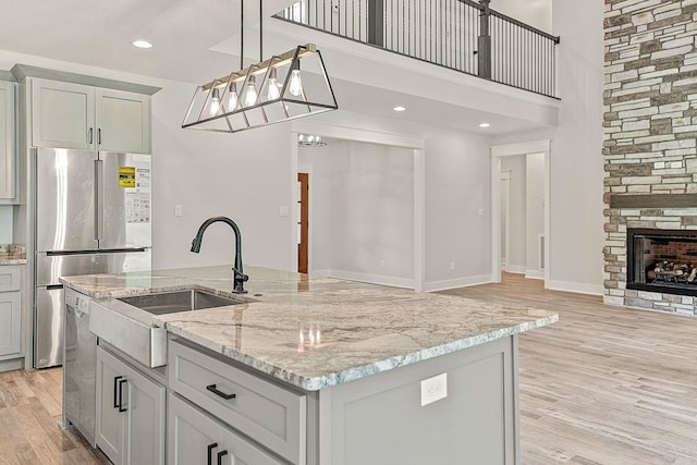 kitchen with hanging light fixtures, light stone countertops, a fireplace, light wood-type flooring, and an island with sink