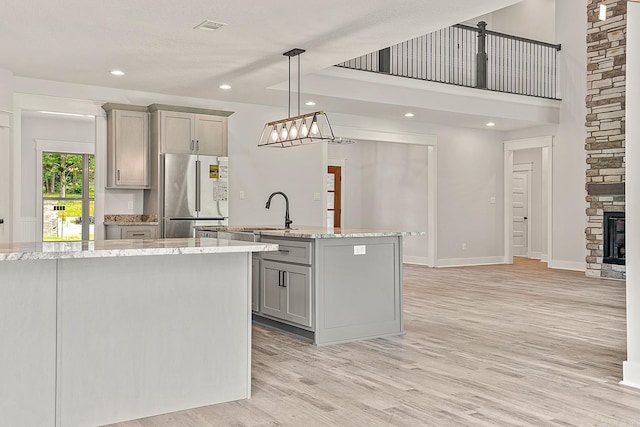 kitchen featuring light wood-type flooring, gray cabinets, stainless steel refrigerator, and hanging light fixtures