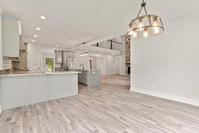 kitchen with gray cabinetry, a center island, hanging light fixtures, light hardwood / wood-style flooring, and stainless steel fridge