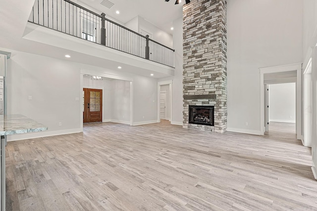 unfurnished living room featuring a stone fireplace, a towering ceiling, and light wood-type flooring