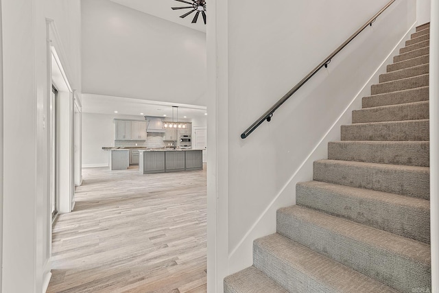 stairway with wood-type flooring, a towering ceiling, and ceiling fan