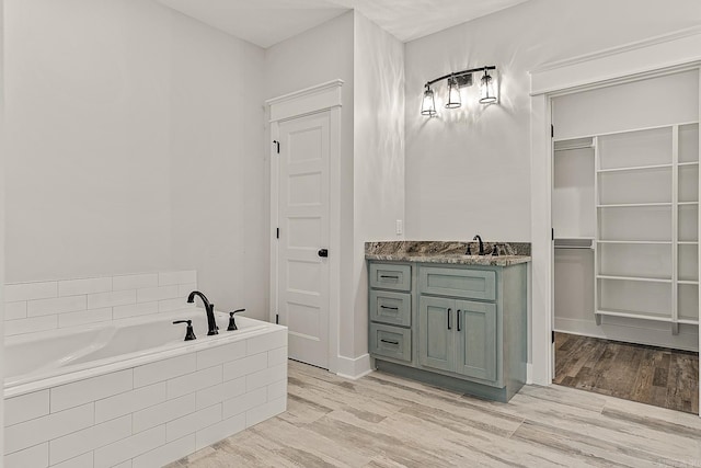 bathroom with hardwood / wood-style floors, vanity, and a relaxing tiled tub