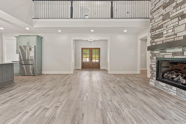 unfurnished living room featuring french doors, light hardwood / wood-style floors, a stone fireplace, and a high ceiling