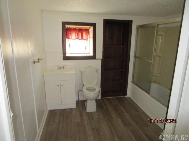 full bathroom with vanity, a textured ceiling, shower / bath combination with glass door, hardwood / wood-style flooring, and toilet