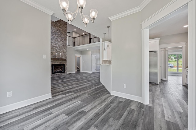 unfurnished living room with dark hardwood / wood-style floors, a notable chandelier, a towering ceiling, a fireplace, and ornamental molding