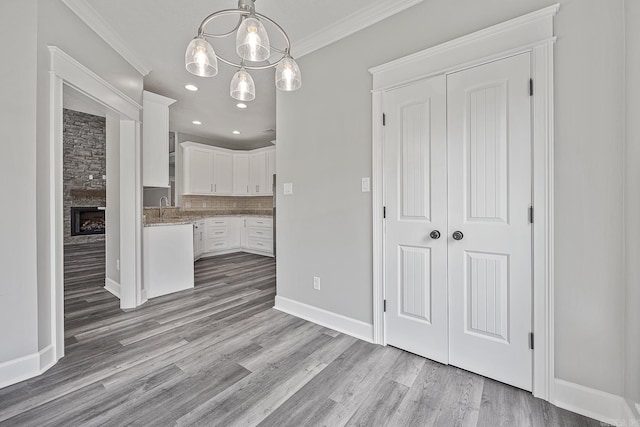 kitchen with decorative light fixtures, white cabinetry, ornamental molding, and light hardwood / wood-style flooring