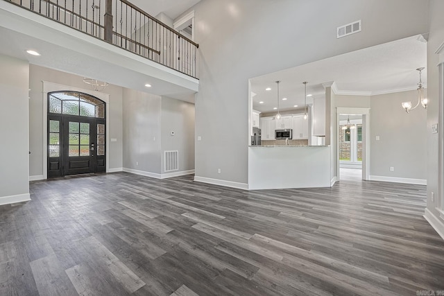 unfurnished living room featuring a towering ceiling, dark hardwood / wood-style floors, crown molding, and a notable chandelier