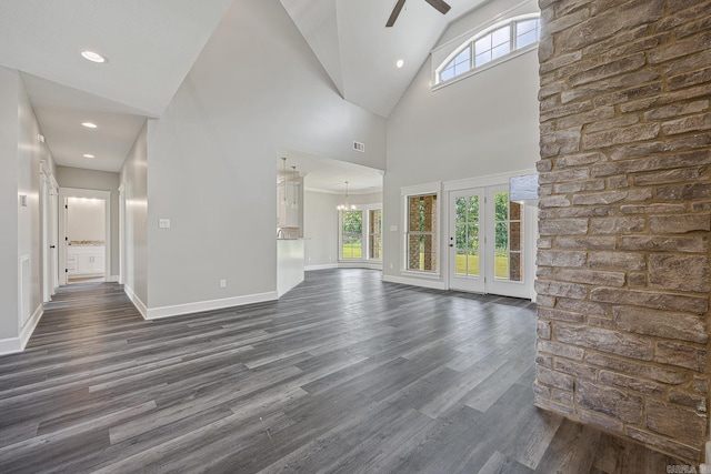 unfurnished living room with dark hardwood / wood-style flooring, plenty of natural light, high vaulted ceiling, and ceiling fan with notable chandelier